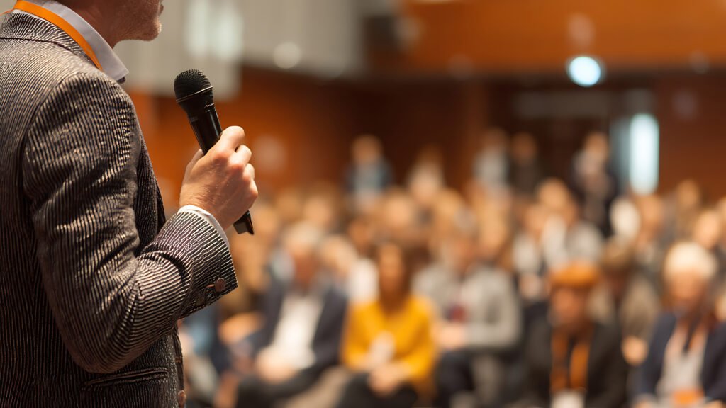 Professional speaker holding microphone addressing a blurred aud